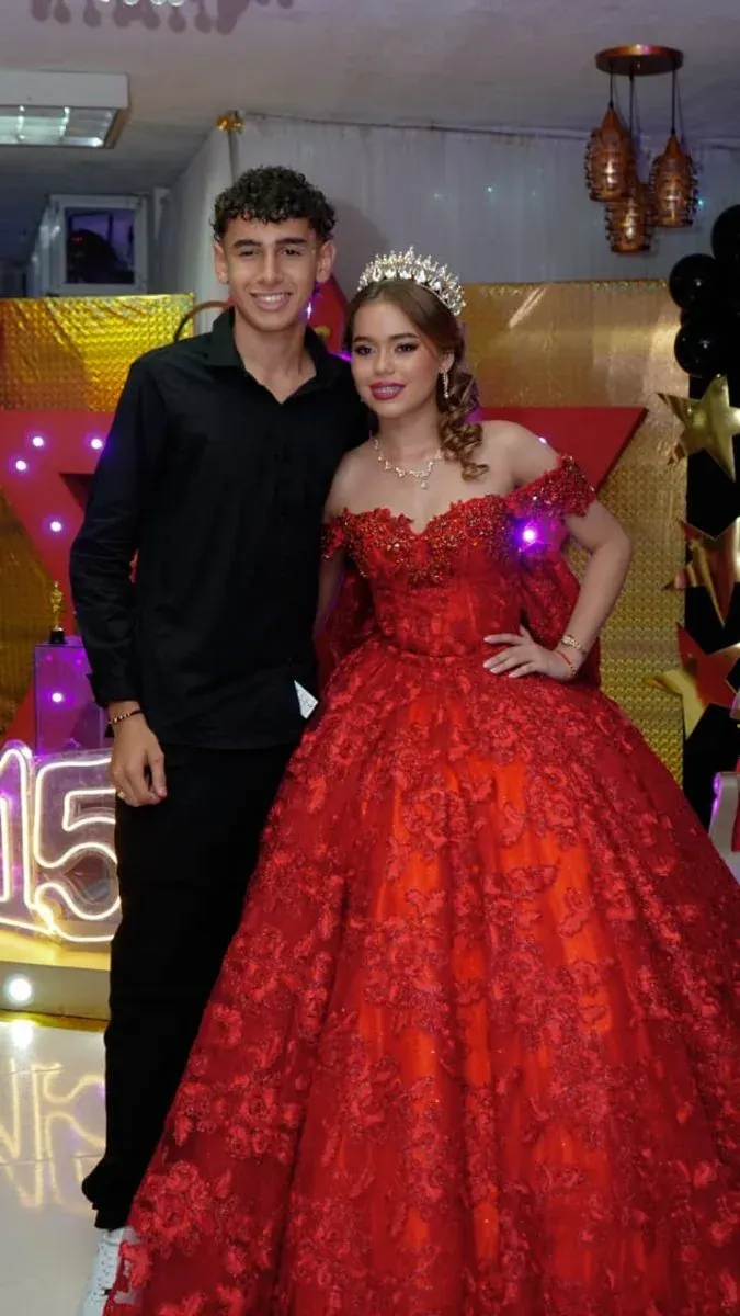 Quinceañera con vestido rojo posando junto a un invitado